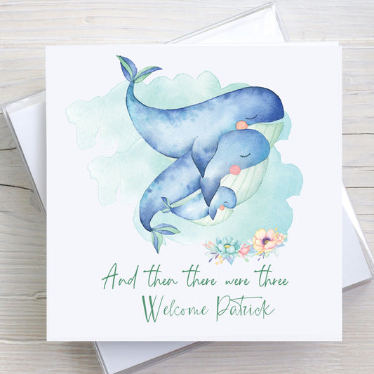Personalised Welcome Baby card showing parent whales embracing a new baby whale. Wording reads "and then there were three" and baby's name.