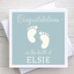 New baby congratulations card featuring baby feet design. Baby name on front. Duck egg coloured background.