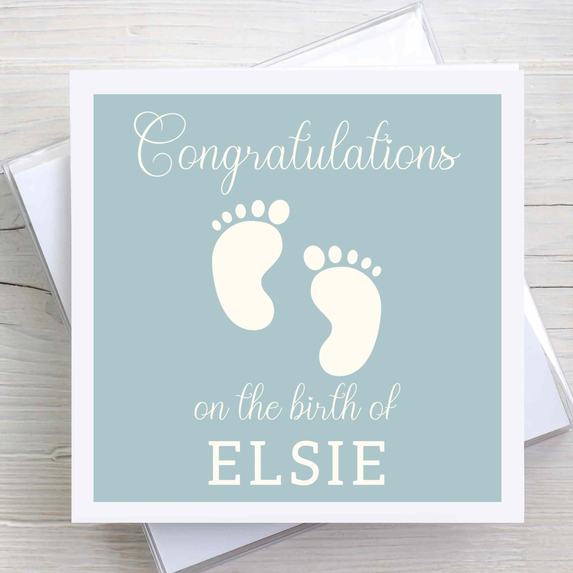 New baby congratulations card featuring baby feet design. Baby name on front. Duck egg coloured background.